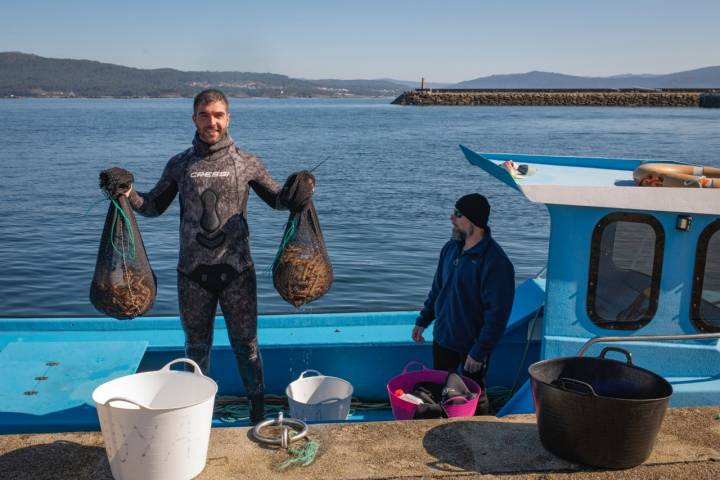 Pescador subido a un barco con dos bolsas de longueirones.