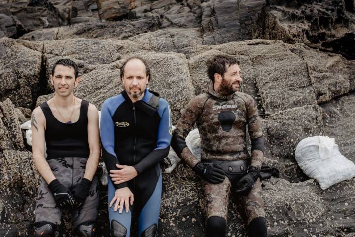 Sergio, Óscar y Alberto, de 'Mar de Ardora', en las rocas de la orilla de la playa al terminar la jornada de recogida de algas, en Galicia.