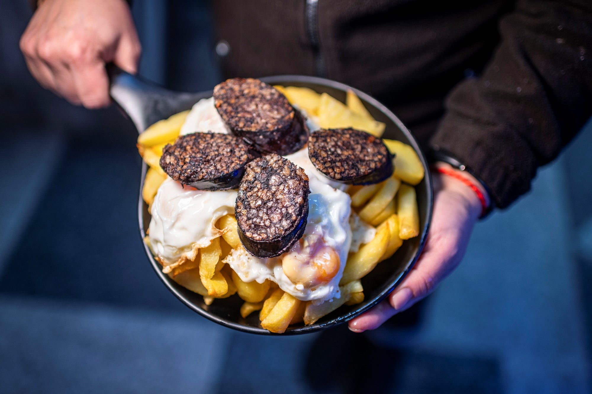 Un plato de patatas con huevos fritos y morcilla.