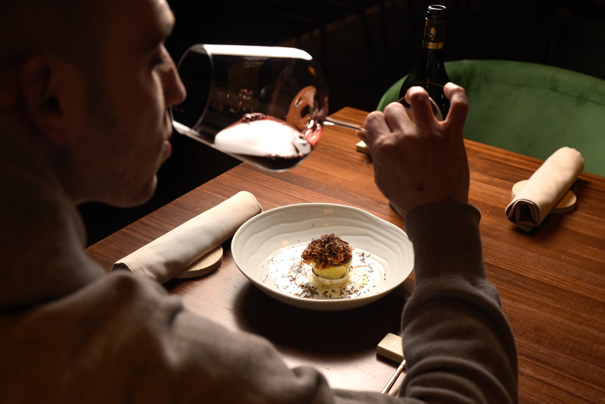 Comensal bebiendo vino con un plato en la mesa.