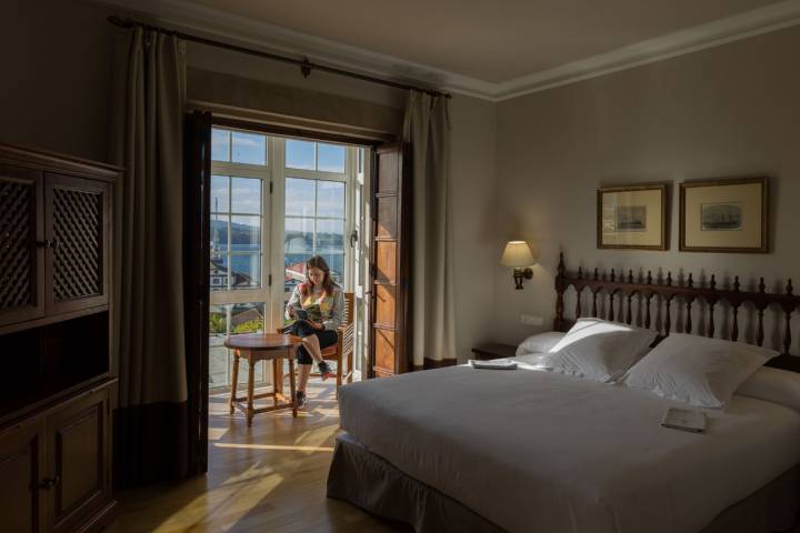 Una mujer lee en la terraza acristalada de una habitación con vistas a la ría de Ferrol.