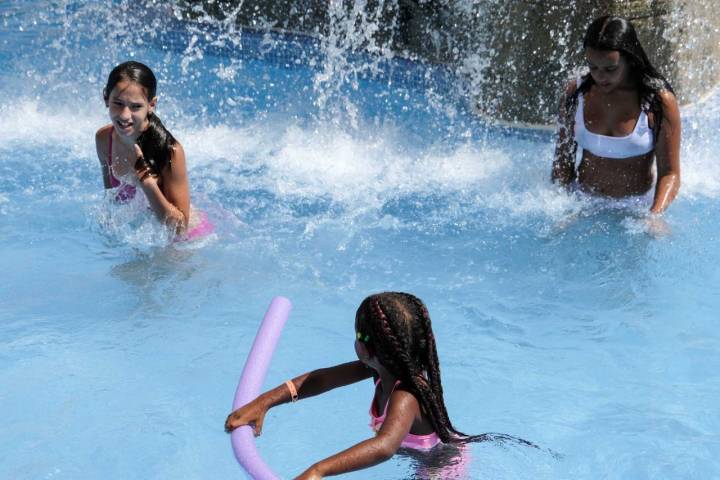 Tres niñas juegan bajo las aguas de una cascada del resort.