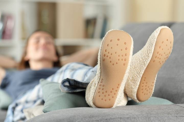 Mujer tumbada en un sofá con zapatillas de estar por casa.