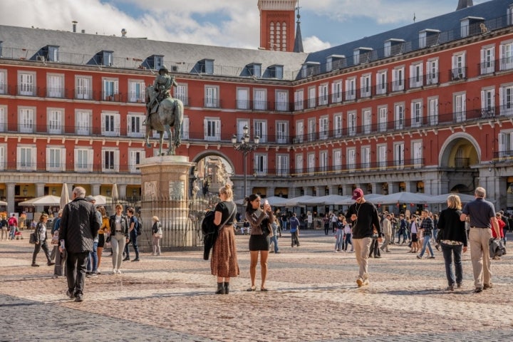 Madrid /Spain - October 14, 2019:  Young women explore and take photos on a busy day in Plaza Mayor, a beautiful and historic plaza in central Madrid. Madrid /Spain - October 14, 2019:  Young women explore and take photos on a busy day in Plaza Mayor, a beautiful and historic plaza in central Madrid.