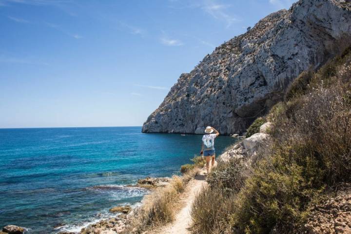Una turista camina con su perro por el sendero que lleva hacia la cala del Peñón de Ifach, en Calpe, Alicante.