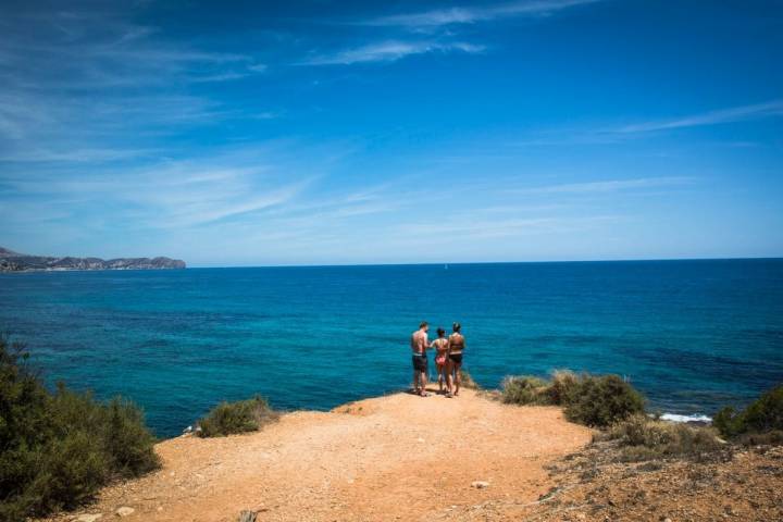 Unos bañistas miran hacia el mar en la cala del Peñón de Ifach, en Calpe, Alicante.